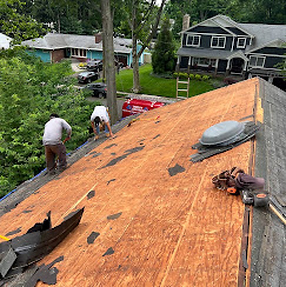 Mid-tear-off showing bare plywood deck and crew working